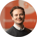 A smiling man in a workshop or garage setting, possibly related to machinery or manufacturing.