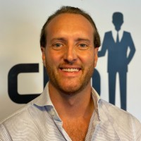 A smiling man in a light-colored shirt standing in front of a CRM logo background, representing consultancy services.