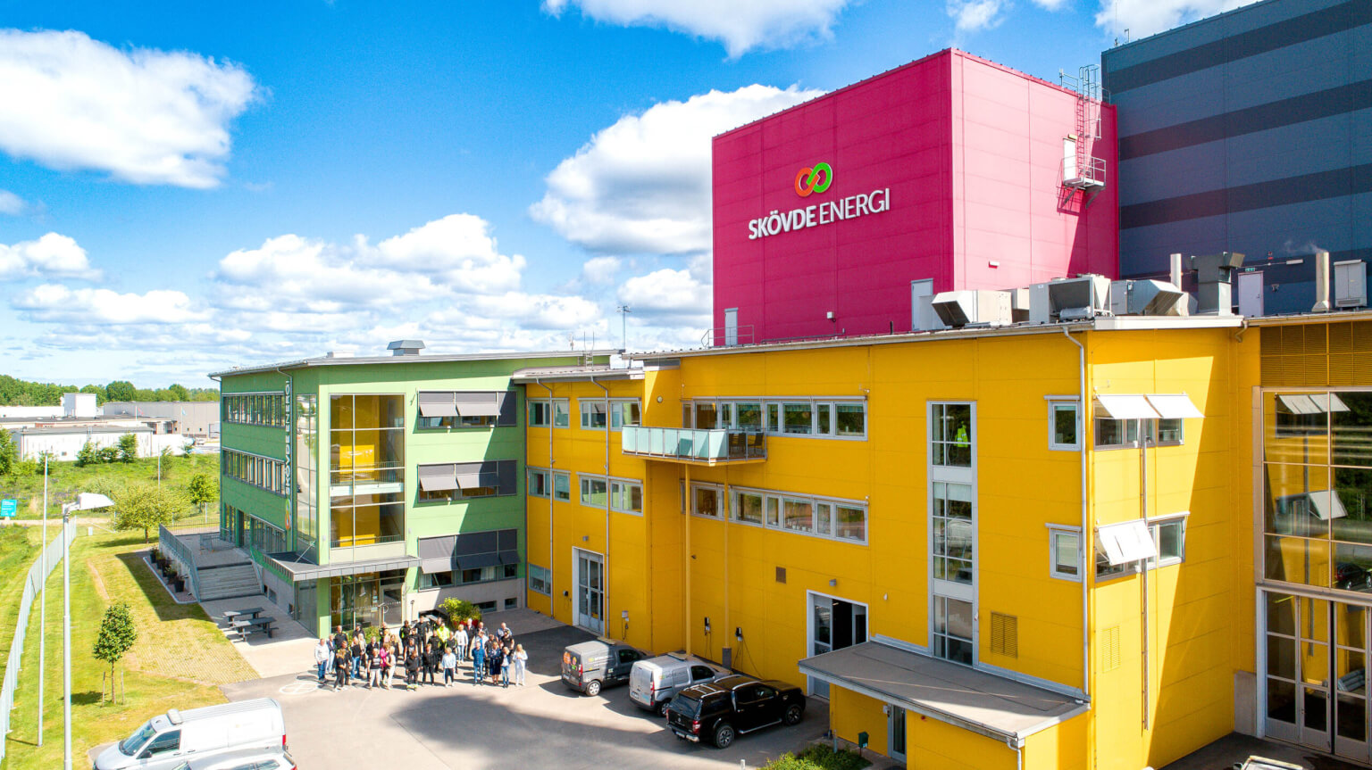 A brightly coloured building complex with yellow, green and pink sections. The pink section on top has a logo on it.