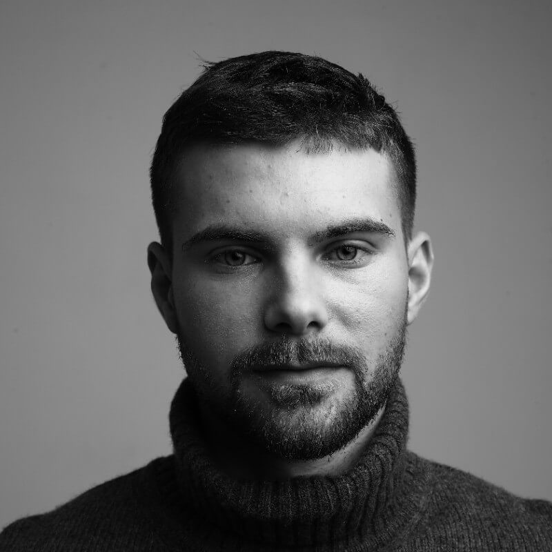 Portrait of a man with short hair and a beard wearing a turtleneck sweater, looking directly at the camera.