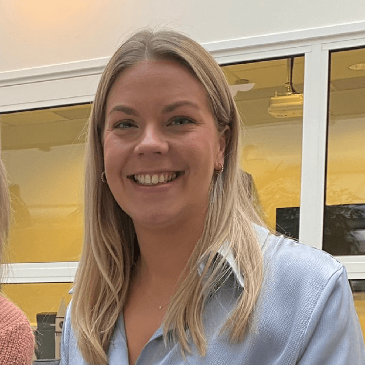 A smiling businesswoman, part of a team or meeting, representing collaboration and consultation in a professional setting.