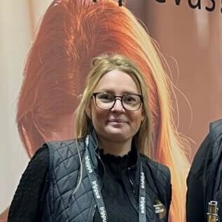 Three people standing behind a wooden table with bread on display at an exhibition, with a backdrop featuring Swedish text.