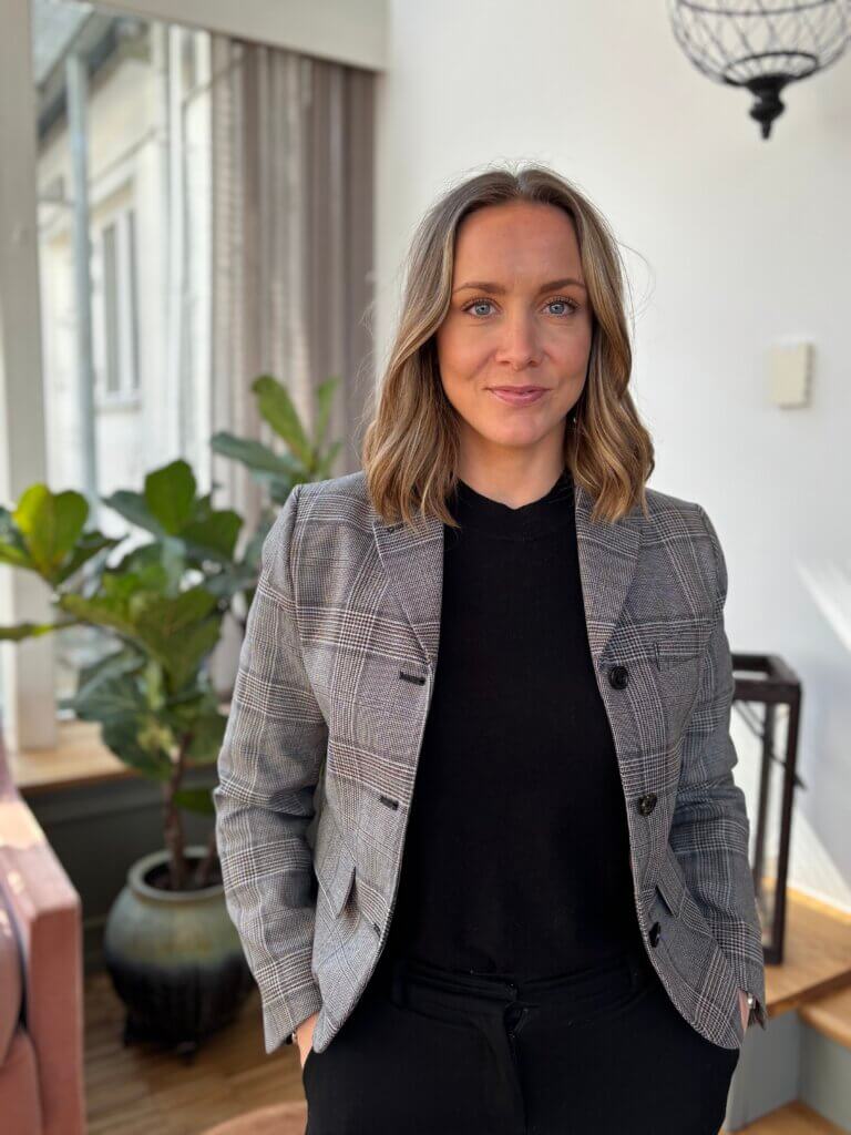 Woman in professional attire standing in a bright room, likely a consultant or real estate agent.