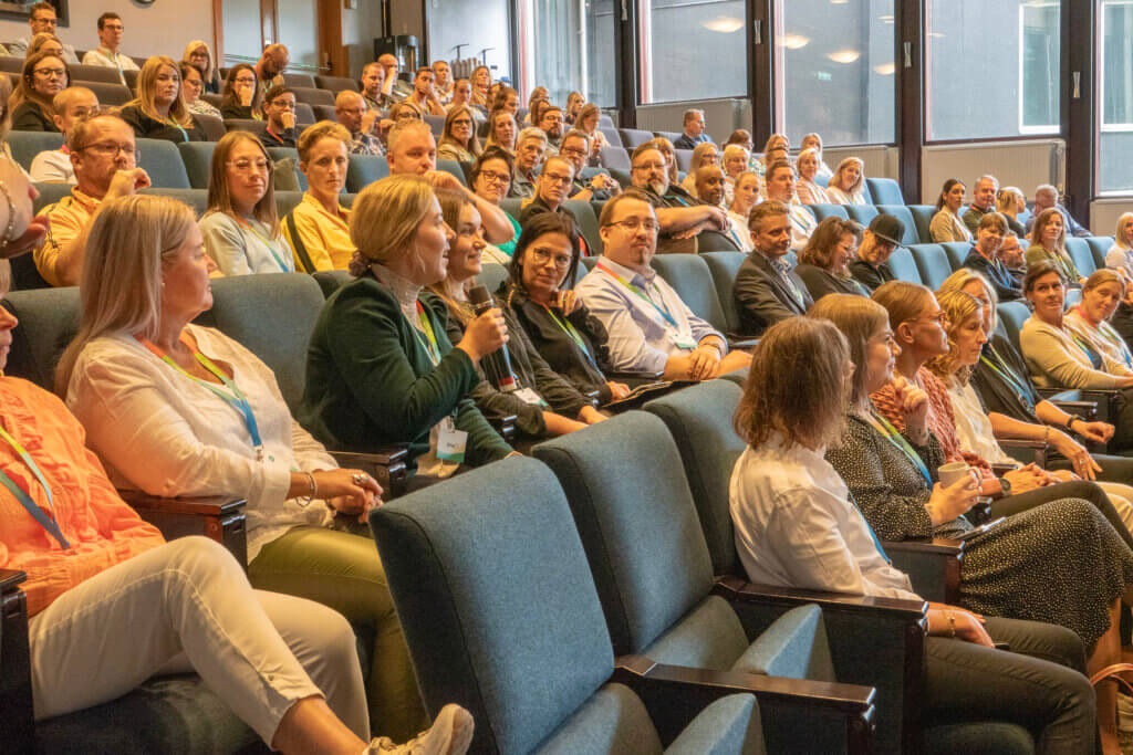 A large audience attentively listening in a conference setting, likely a seminar or workshop related to CRM solutions.