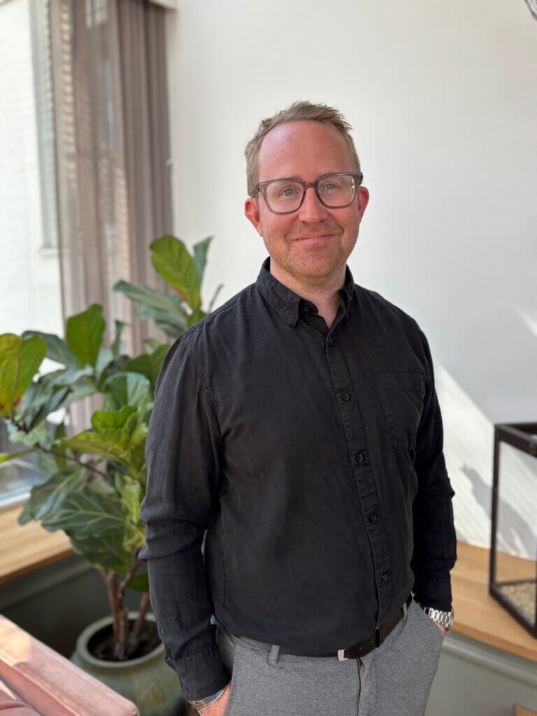 A man in office attire standing in front of a potted plant