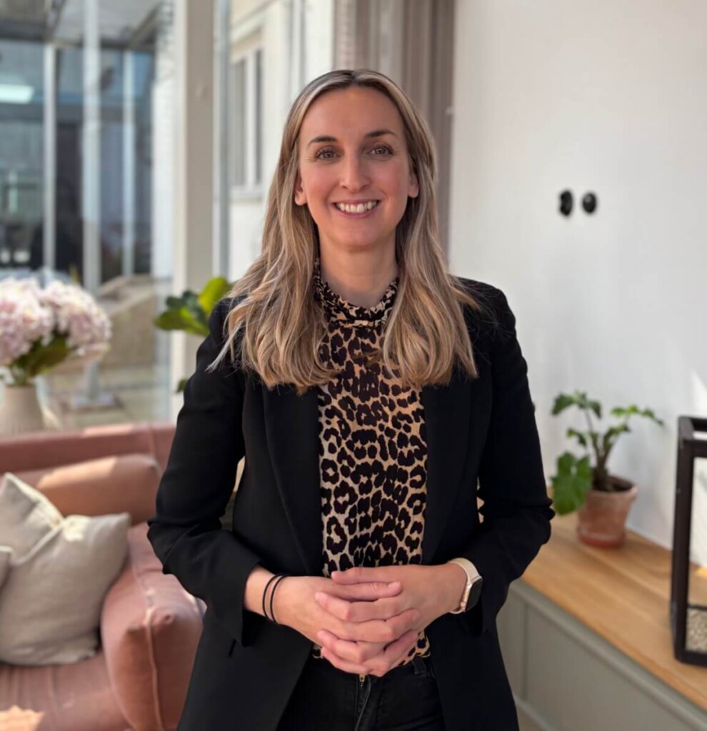 Smiling businesswoman standing in a modern office with natural light, representing consultancy and CRM solutions.