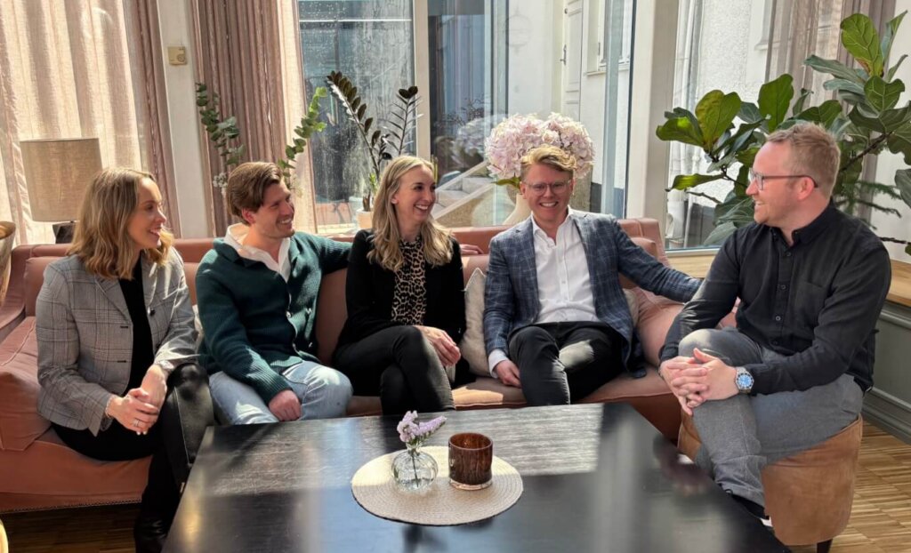 Group of business professionals engaged in a meeting or discussion in a modern office setting, sitting around a coffee table.
