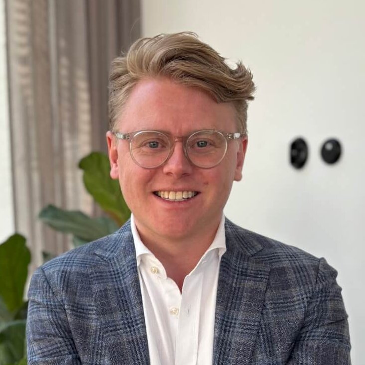Smiling man in a plaid blazer standing in a modern office with plants