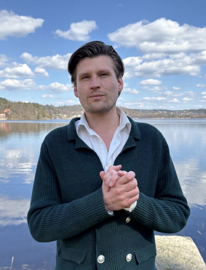 A man in a cardigan standing by a serene lake, conveying a sense of calm and professionalism, suitable for a CRM consultancy profile.