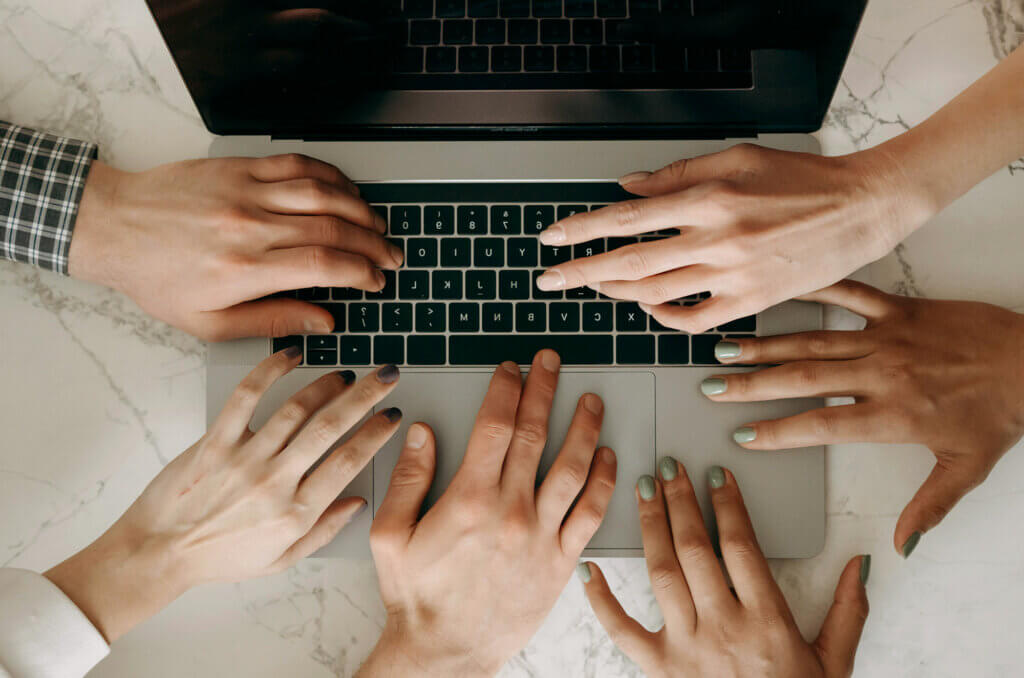 Hands of diverse team members collaborating on a laptop keyboard, symbolizing cooperation and teamwork in achieving a common goal.