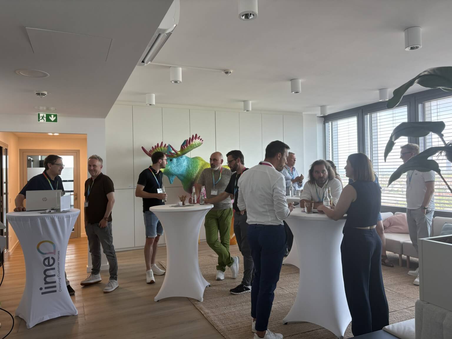 A group of people standing around tables in a networking event, possibly a CRM conference or meeting. The room has a modern interior with a globe decoration.