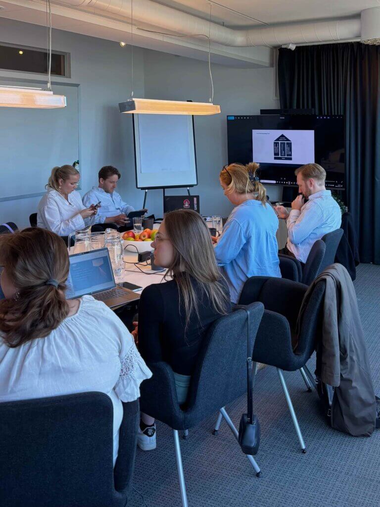A group of professionals engaged in a CRM strategy workshop. The team collaborates around a table with laptops, discussing customer relationship solutions for sectors like real estate or utilities.