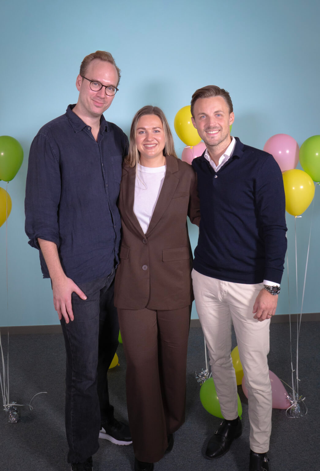 Smiling business team members standing together in a corporate office. Celebratory balloons in the background suggest a successful CRM project completion or company milestone.